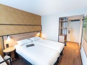 Une chambre d’hôtel moderne équipée d’un lit, de tables de chevet, d’un bureau et d’une bibliothèque intégrée.