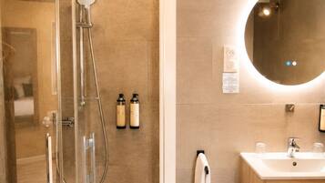 Een moderne badkamer met een glazen douchecabine, een houten wastafelmeubel met spiegel en een handdoekrek.