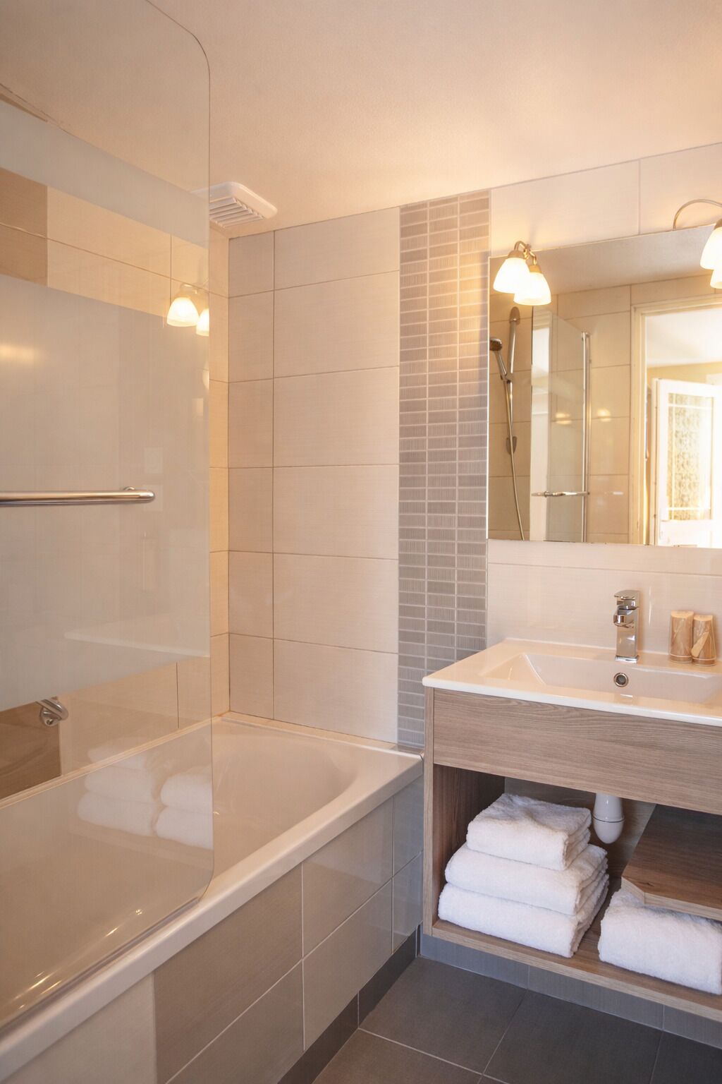 Une salle de bain moderne équipée d’une baignoire, d’une douche, d’un meuble-lavabo avec un miroir et d’un porte-serviettes.