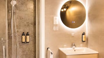 Een moderne badkamer met een douchecabine van glas, een houten wastafelmeubel met een ronde spiegel en een handdoekhouder.