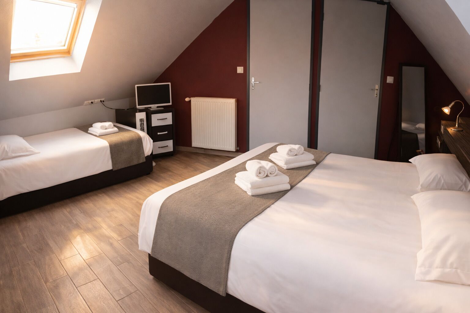 Una habitación de hotel con dos camas, televisión, cómoda, radiador y tragaluz.
