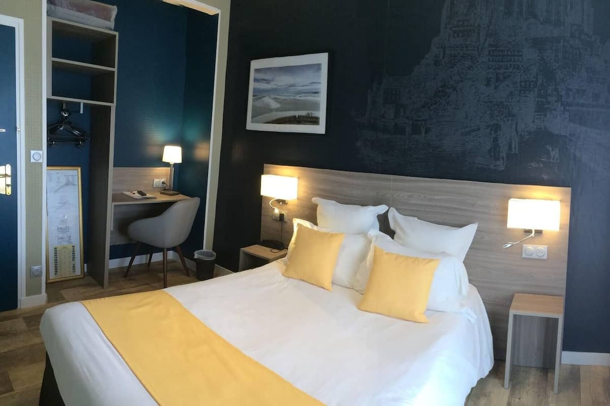 A hotel room with a bed, bedside lamps, a desk, and a chair.