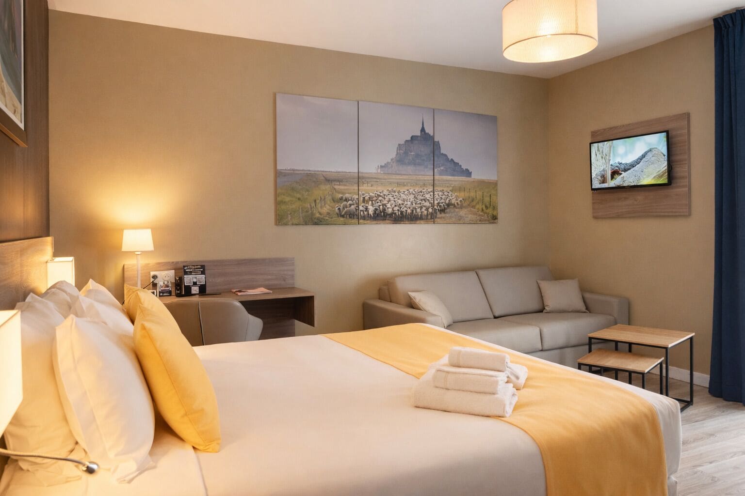 Una habitación de hotel con cama, escritorio, sofá, televisor y obras de arte en las paredes.