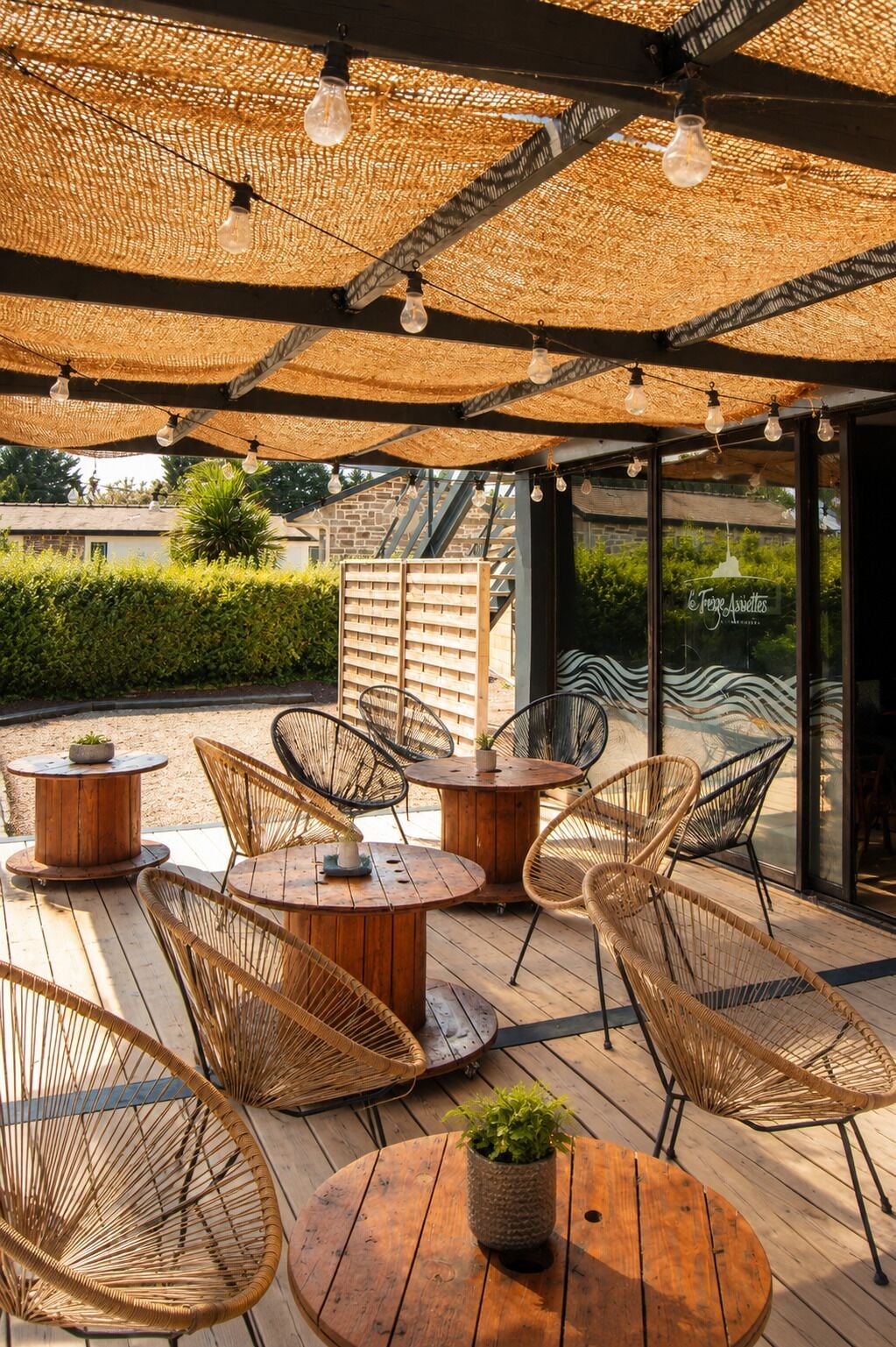 An outdoor seating area with wicker chairs and tables, a thatched roof, and a view of the surrounding landscape.