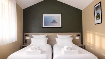 Habitación de hotel con dos camas, una pared de acento verde oscuro, un cuadro enmarcado sobre las camas y una ventana con cortinas blancas.