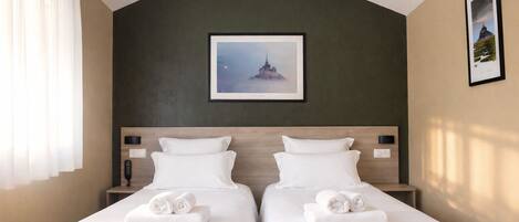 Habitación de hotel con dos camas, una pared de acento verde oscuro, un cuadro enmarcado sobre las camas y una ventana con cortinas blancas.