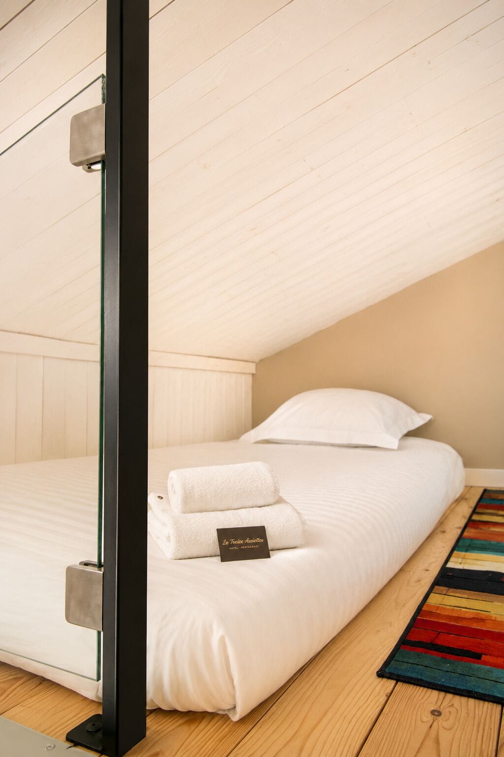 A single bed with white bedding, a small bedside table, and a colorful rug.
