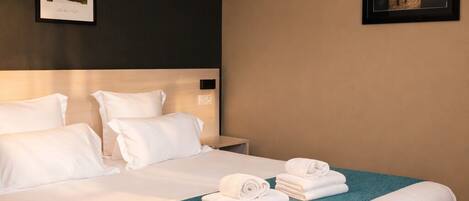 A hotel room with a large bed, a headboard, a nightstand, and two framed pictures on the walls.