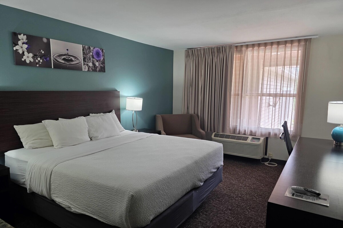 Una habitación de hotel con una cama, una silla, un escritorio con lámpara y una ventana con cortinas.
