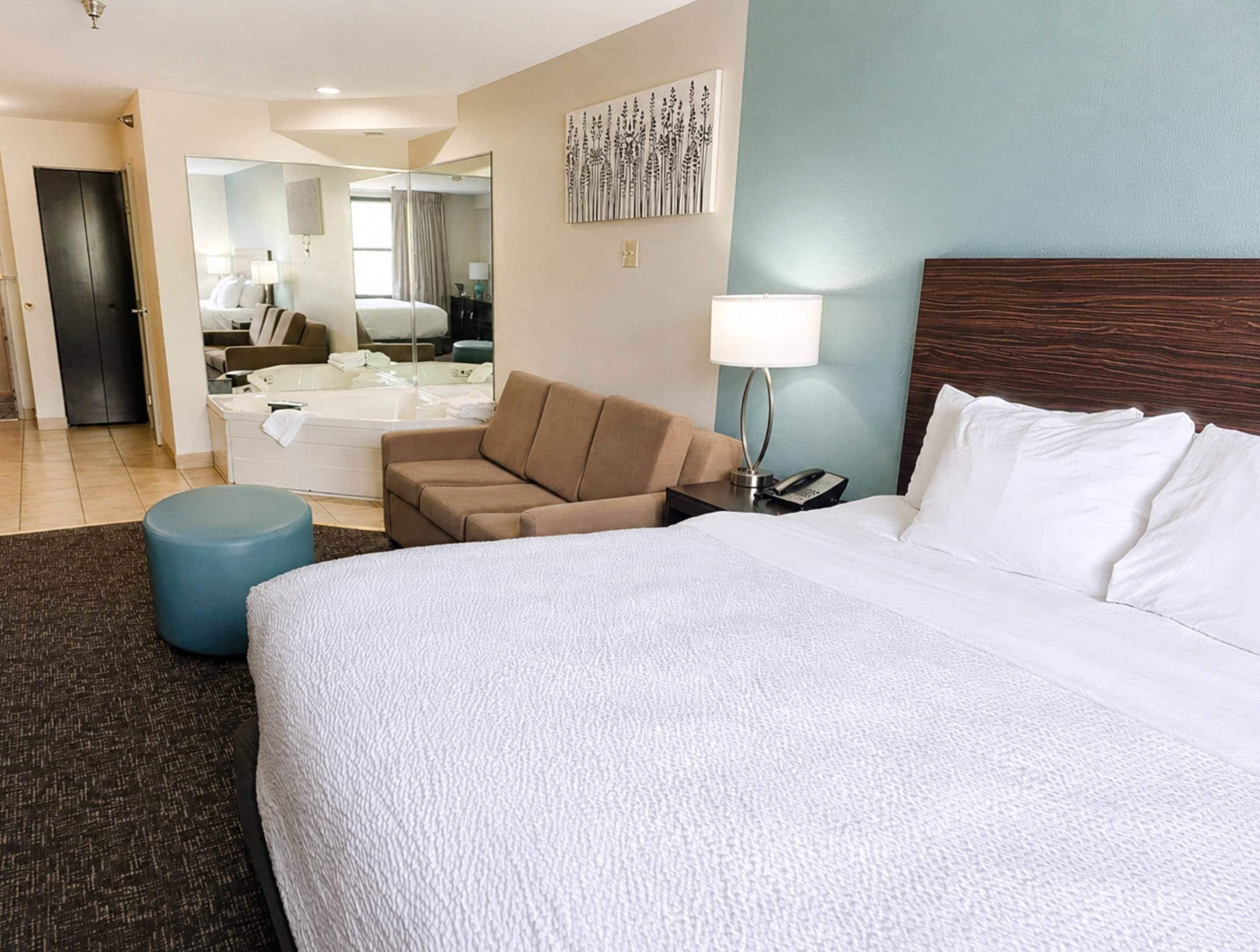 Habitación de hotel con una cama grande, un sofá, un escritorio con una lámpara, un teléfono y un baño con bañera y espejo.