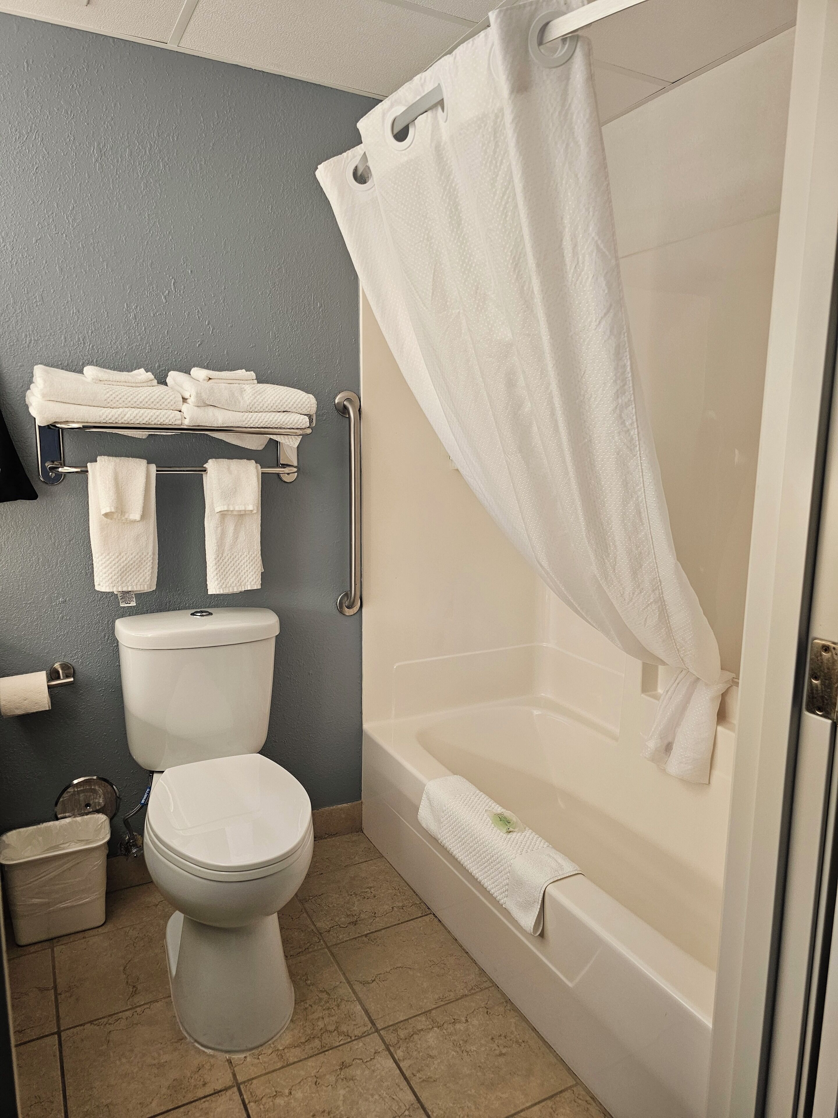 Un baño con inodoro, bañera, cortina de ducha y toallero con toallas dobladas.