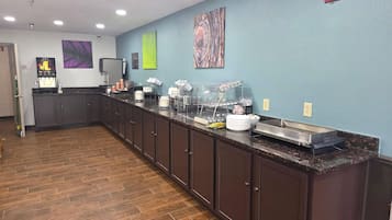 A long counter with various food and beverage dispensers, a coffee machine, and a trash can.