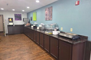 Una larga barra con varios dispensadores de comida y bebida, una máquina de café y un bote de basura.