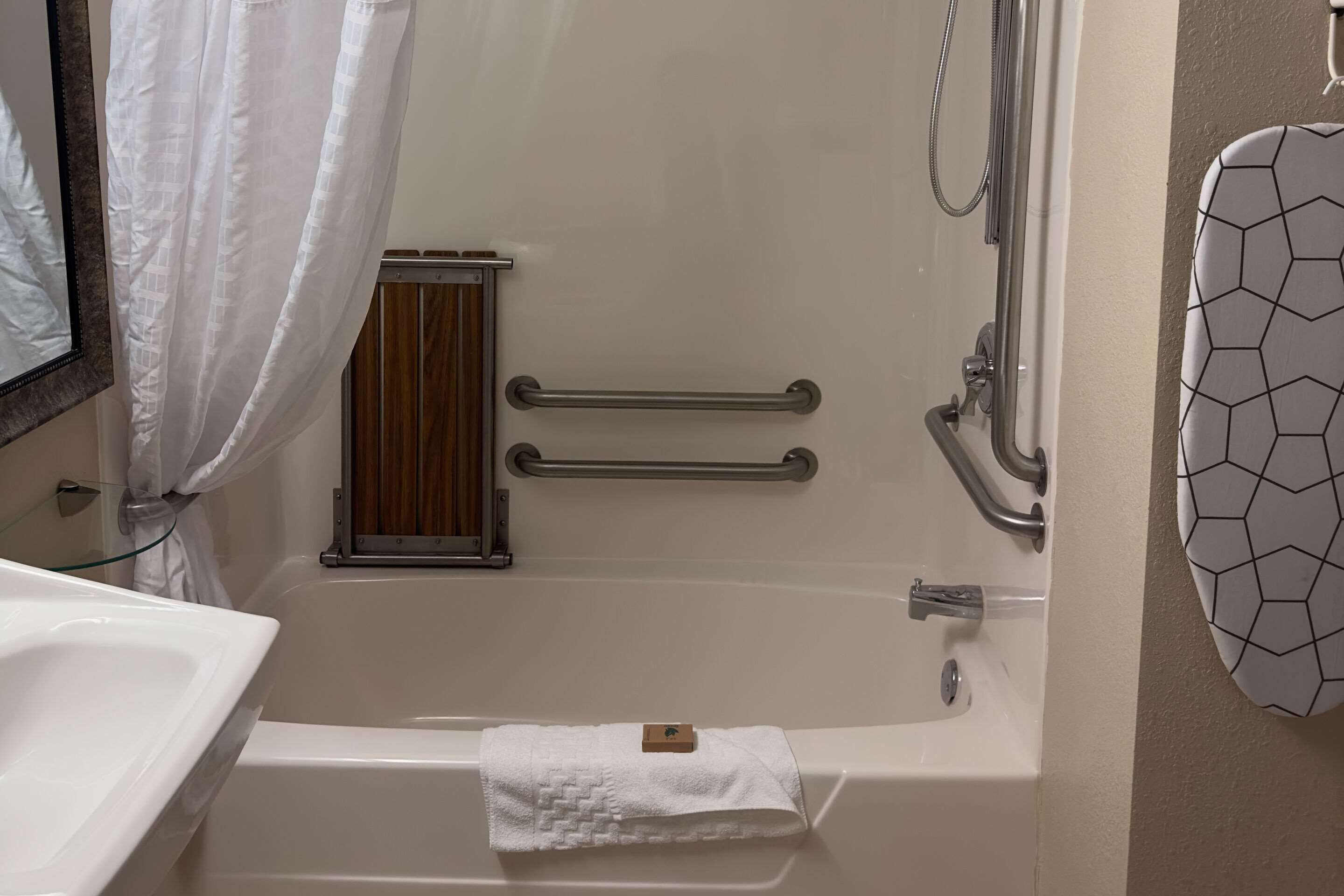 A bathroom with a bathtub, a shower, a handrail, a towel, and a mirror.