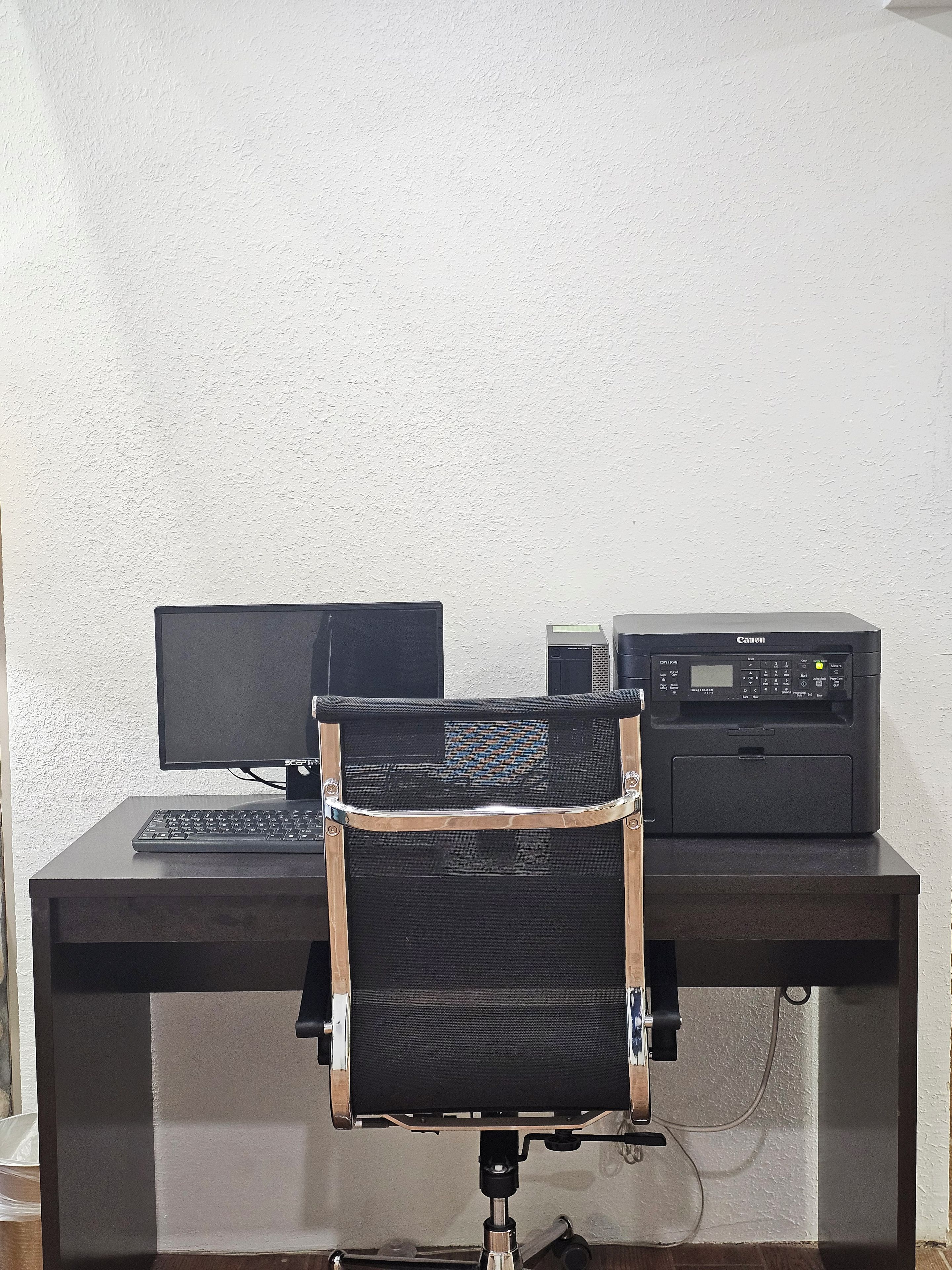 Een werkplek met een beeldscherm, toetsenbord en een printer op een bureau.
