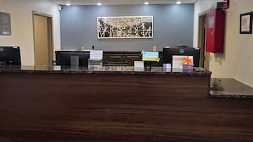 Un mostrador de recepción de hotel con una computadora, un letrero para tarjetas de acceso y un cuadro en la pared.