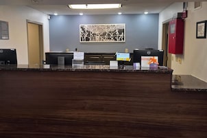Un mostrador de recepción de hotel con una computadora, un letrero para tarjetas de acceso y un cuadro en la pared.