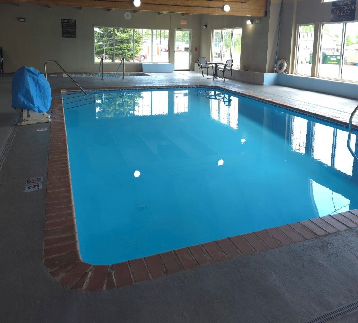 An indoor swimming pool with a clear blue water surface, surrounded by a brick edge and a tiled floor.