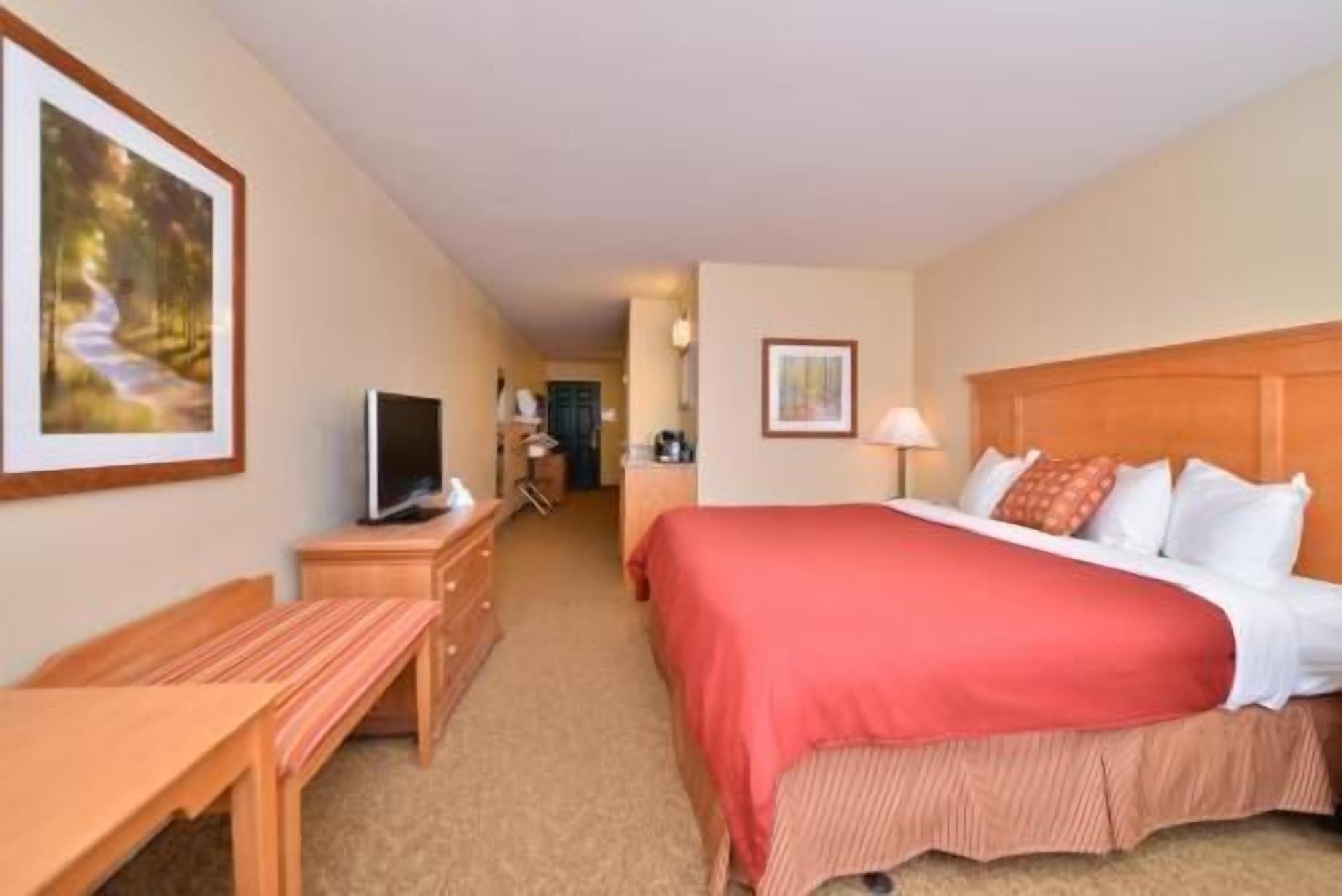 A hotel room with a bed, a desk, a television, and a painting on the wall.