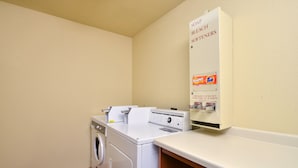 A laundry area with a washing machine, dryer, and a soap dispenser on the wall.