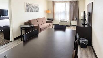 A hotel room with a sofa, a dining table, a TV, and a window with curtains.