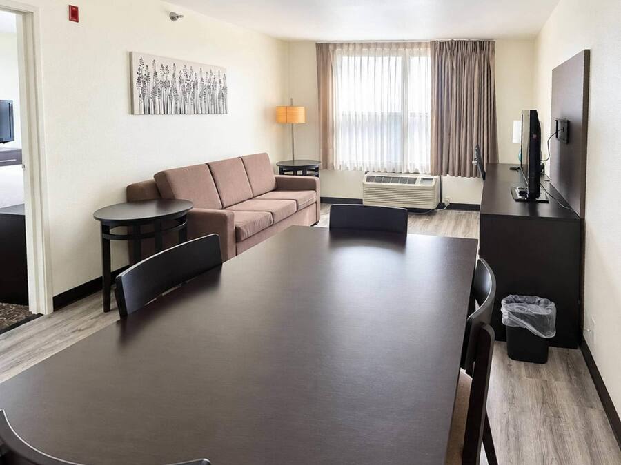 A hotel room with a sofa, a dining table, a TV, and a window with curtains.