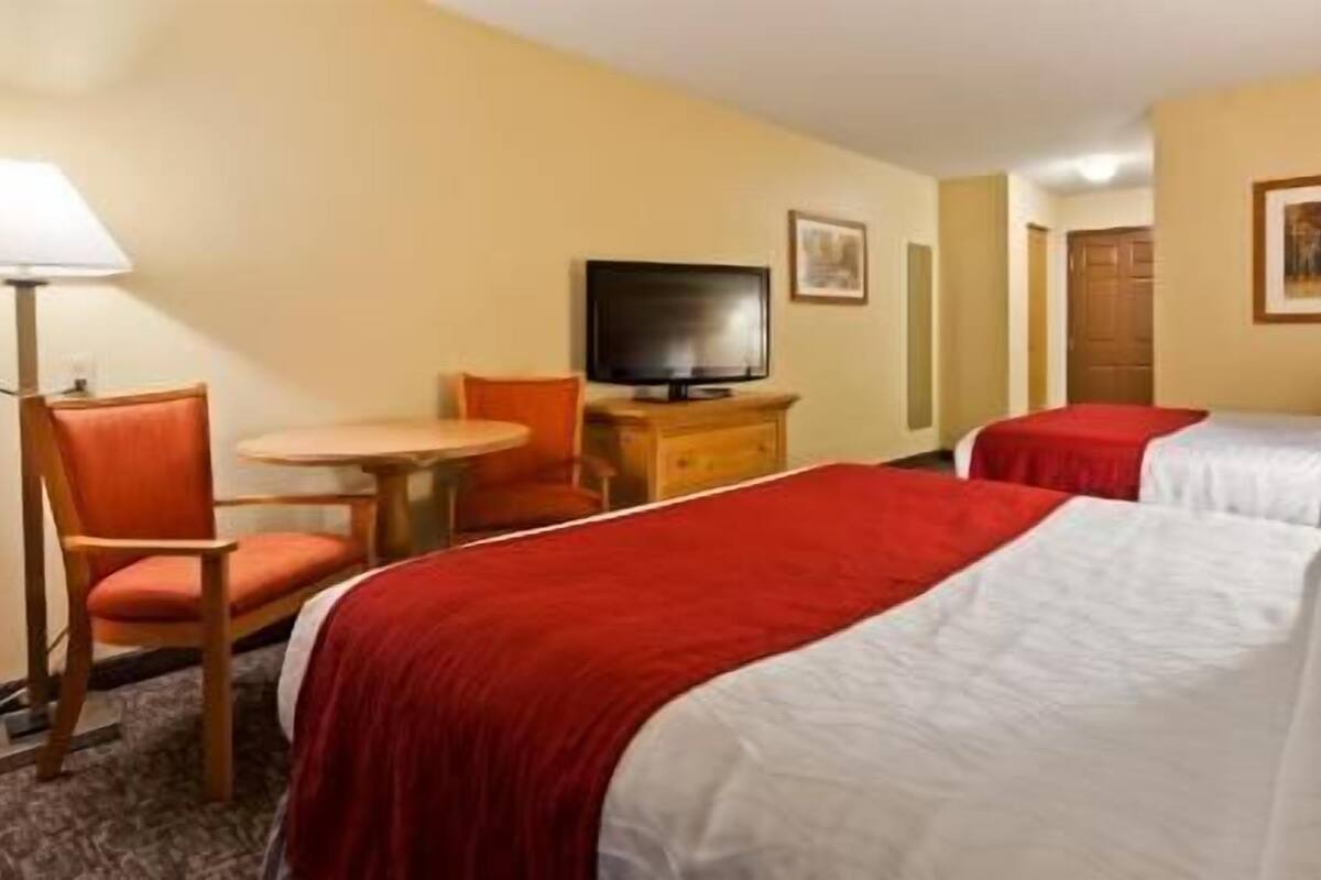 A hotel room with two beds, a TV, a desk, and a chair.