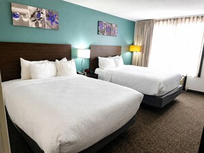 Habitación de hotel con dos camas, un reloj, una lámpara y una obra de arte en la pared.