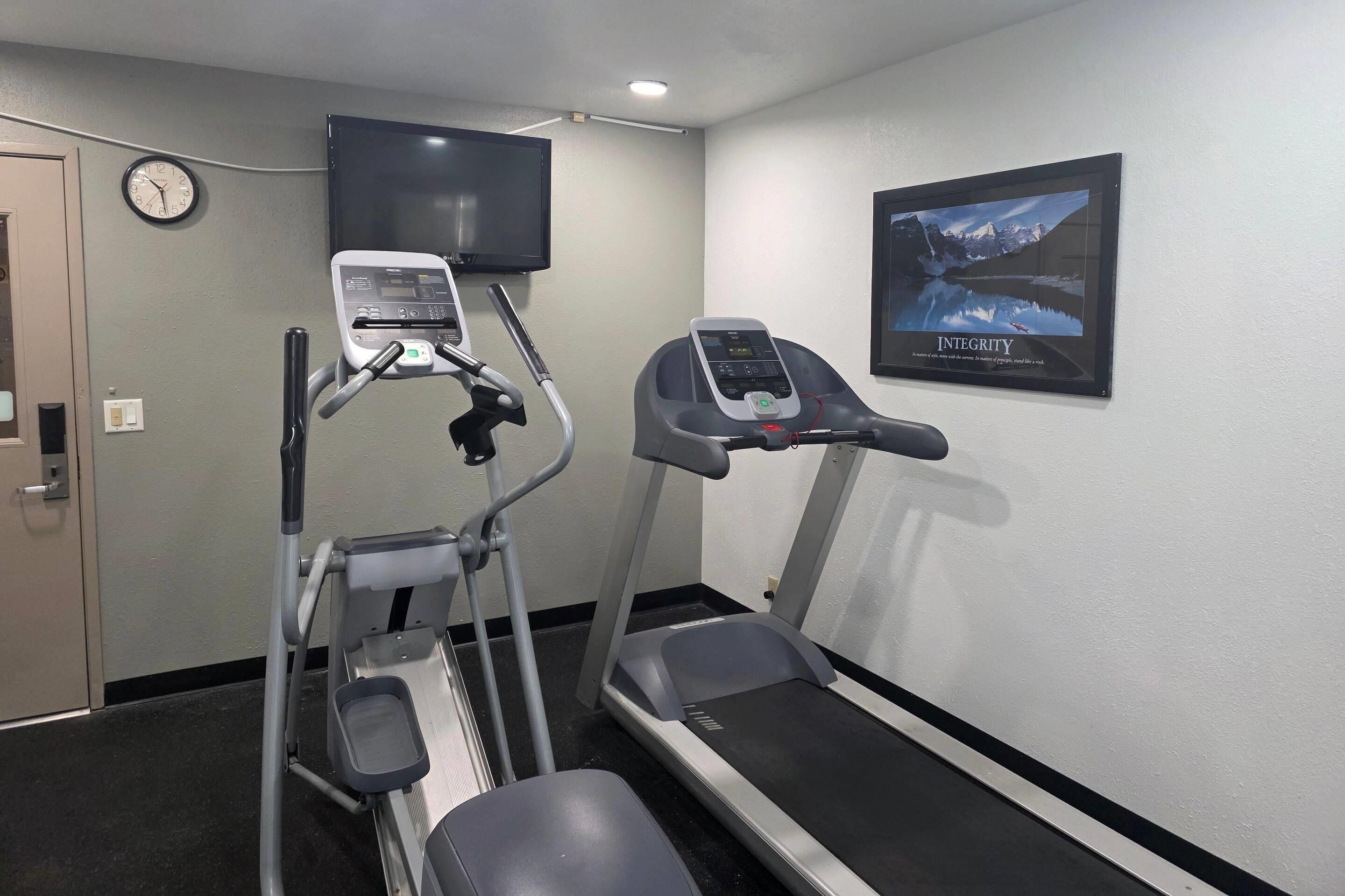 A gym with treadmills and an elliptical machine, a clock, and a motivational poster on the wall.