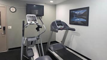 Une salle de sport équipée de tapis de course et d’un appareil elliptique, avec une horloge et une affiche motivante accrochée au mur.