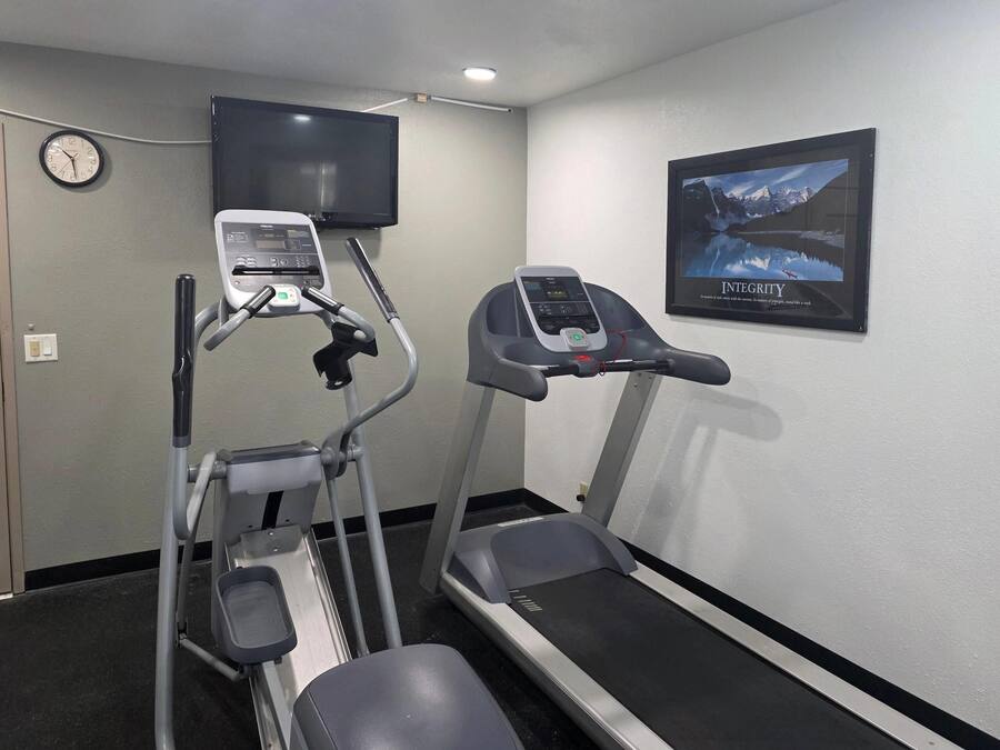 Une salle de sport équipée de tapis de course et d’un appareil elliptique, avec une horloge et une affiche motivante accrochée au mur.