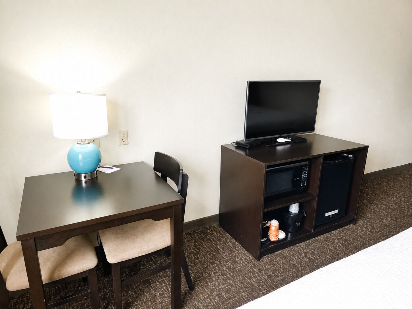 Habitación de hotel con escritorio, silla, lámpara, televisión y minibar.