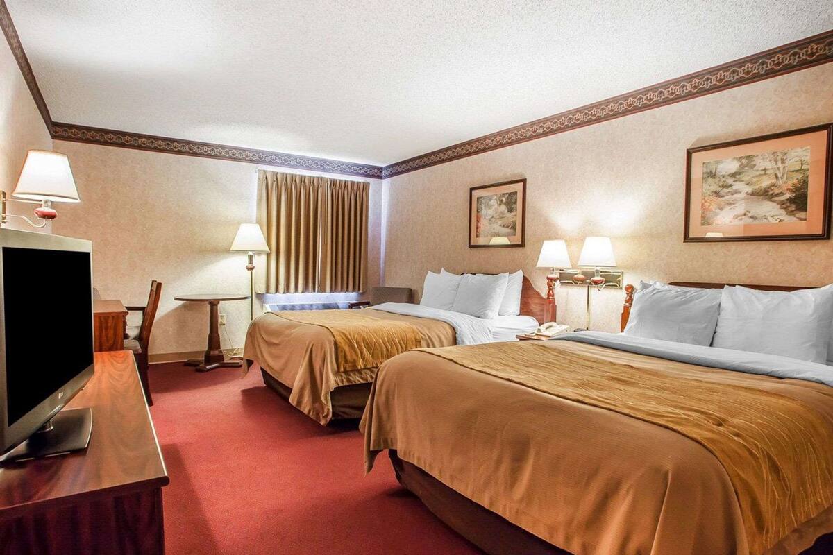 Habitación de hotel con dos camas, televisor, escritorio y dos lámparas.