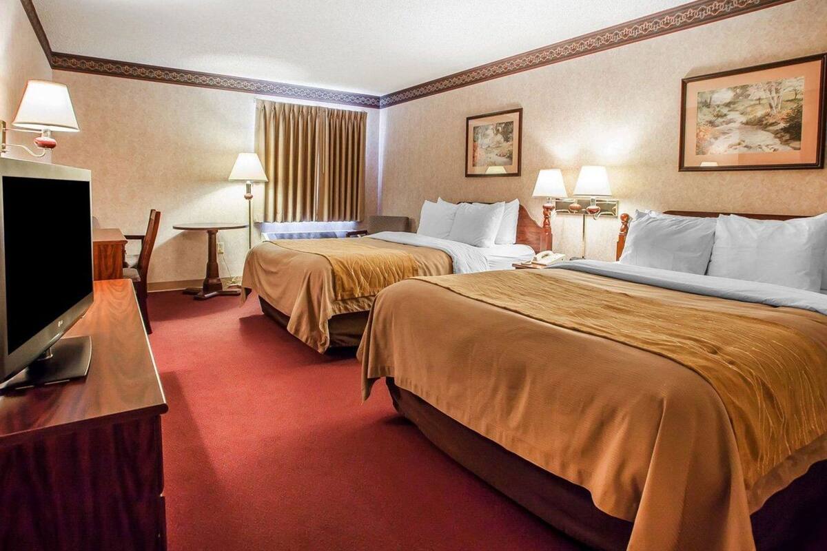 Habitación de hotel con dos camas, televisión, escritorio y lámparas.