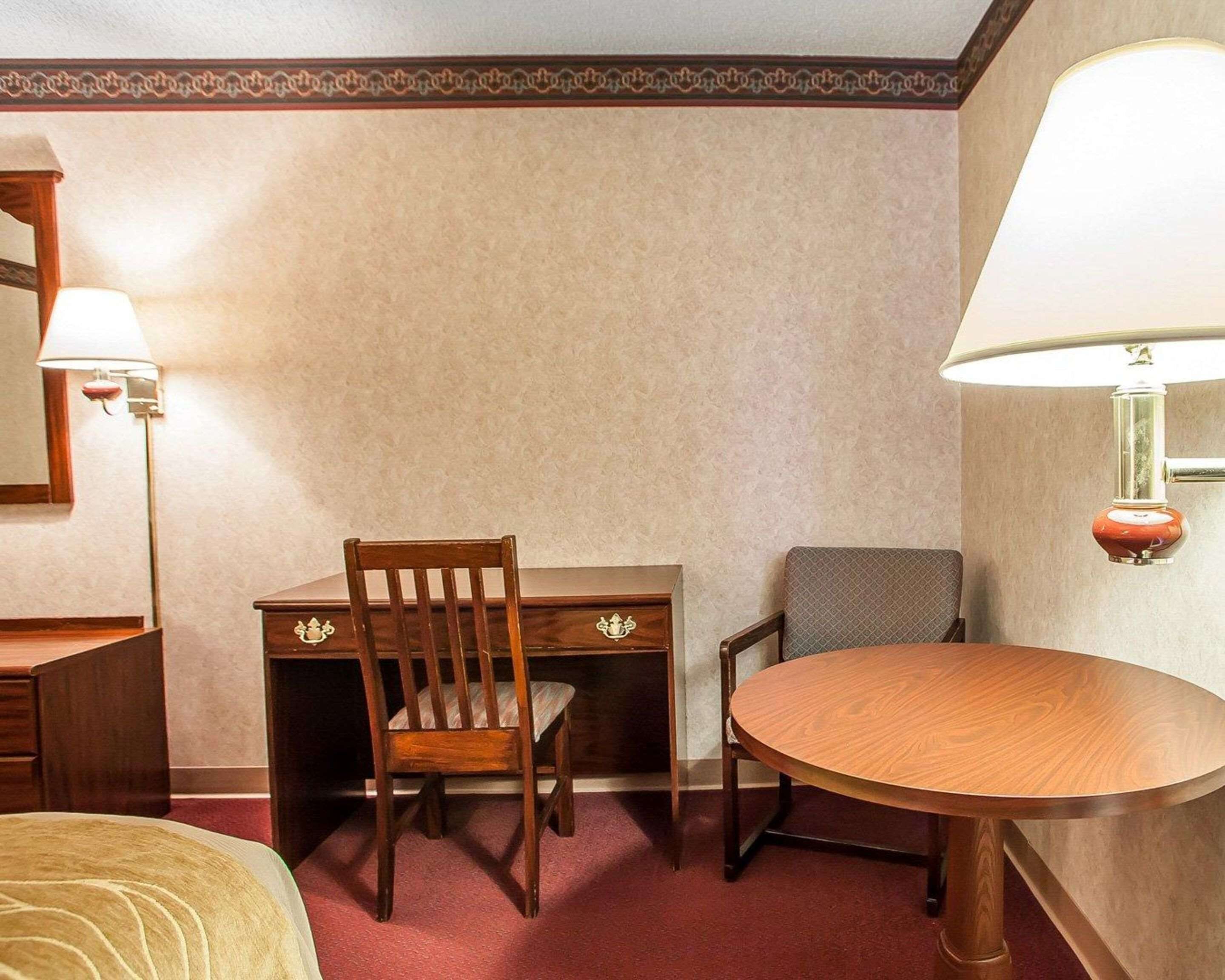 A hotel room with a bed, a desk with a chair, a round table, and two wall-mounted lamps.