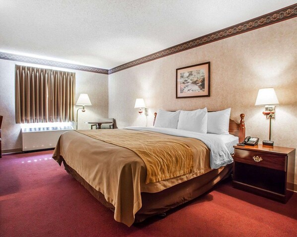 A hotel room with a large bed, two bedside tables with lamps, a window with curtains, a radiator, and a painting on the wall.