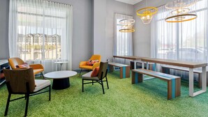 A modern lounge area with a green carpet, wooden furniture, and large windows with sheer curtains. - Spark by Hilton Daleville Roanoke North (Daleville)