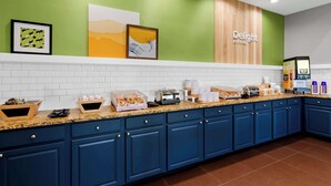 A modern kitchen with blue cabinets, a granite countertop, and a wall-mounted coffee machine. - Spark by Hilton Daleville Roanoke North (Daleville)