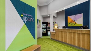 A reception area with a wooden counter, a bench, and a wall with geometric patterns and a sign that reads "It only takes a spark." - Spark by Hilton Daleville Roanoke North (Daleville)