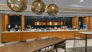 Una cocina moderna con encimera de madera, zona de comedor con una mesa larga y sillas, y lámparas colgantes hexagonales decorativas.
