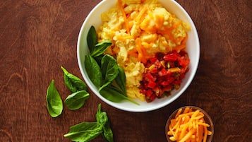A bowl of scrambled eggs with cheese and bell peppers on a wooden table.