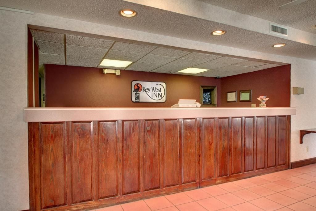 A reception desk with a wooden panel design, a sign for 'Key West Inn,' and a tiled floor.