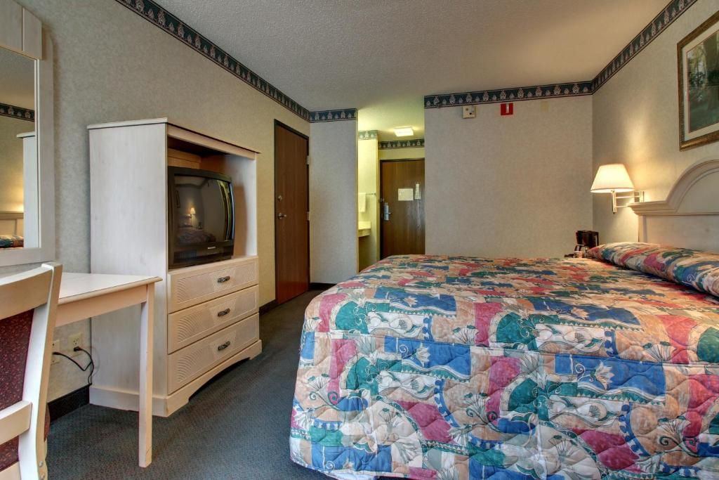 Una habitación de hotel con una cama, un escritorio, un televisor y una puerta que da a un baño.