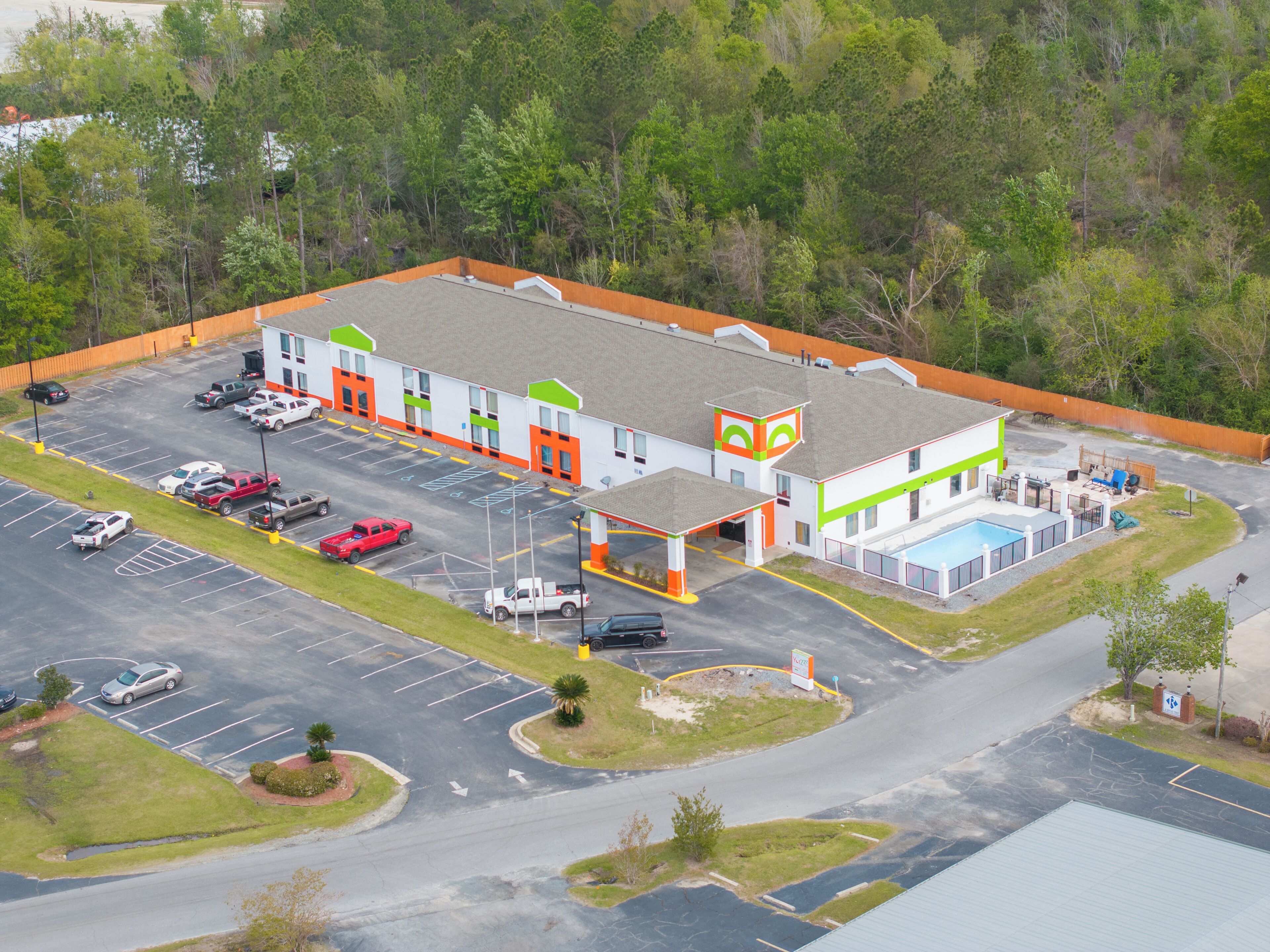 A multi-story building with a parking lot, a swimming pool, and a fenced area.