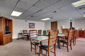 A conference room with a large table, multiple chairs, a television, and a kitchenette area.