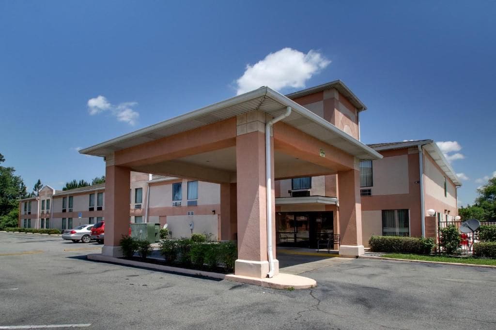A hotel with a covered entrance, multiple windows, and a parking lot with cars.