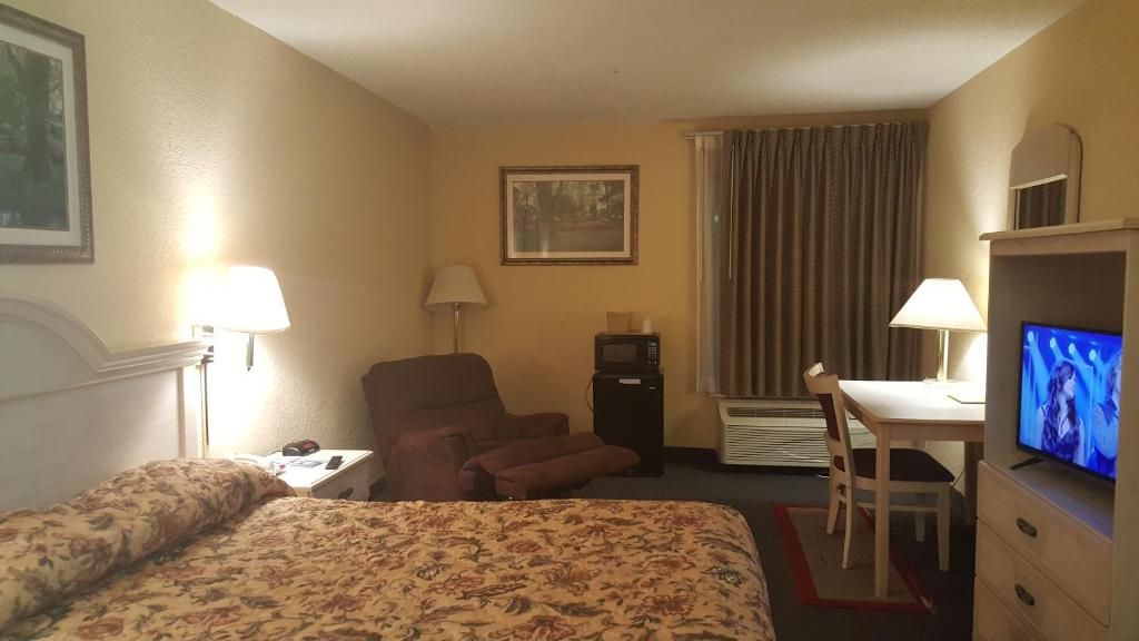 Hotelkamer met een bed, bureau, stoel, televisie, magnetron en raam met gordijnen.
