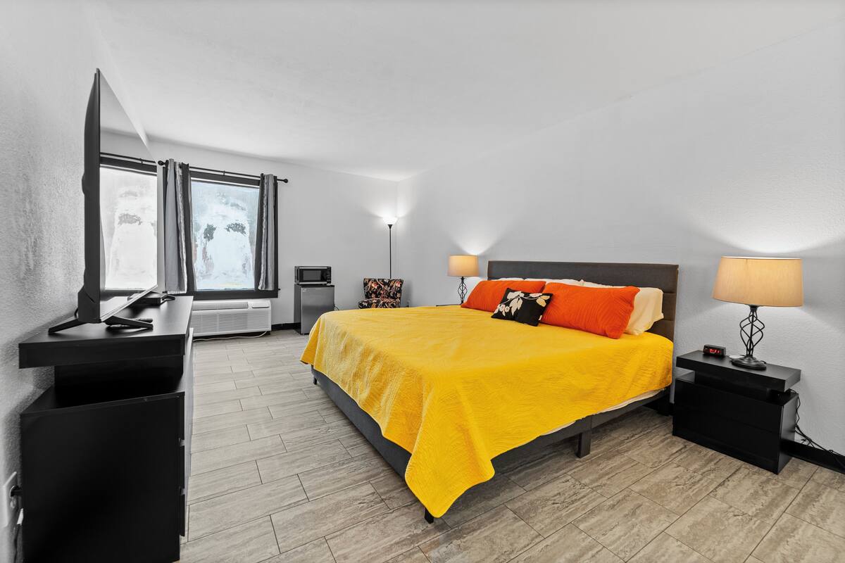 Ein modernes Hotelzimmer mit Bett, Nachttischen, Schreibtisch, Stuhl, Lampe und Fenster.