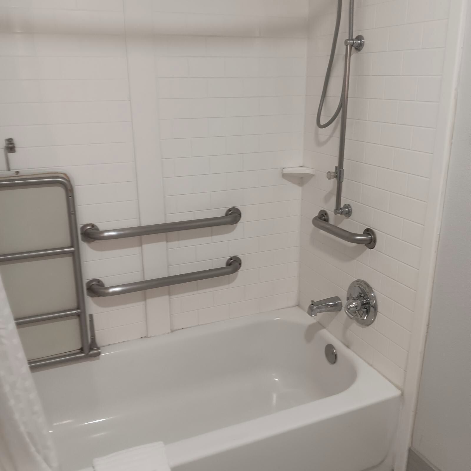 Une salle de bain avec une baignoire blanche, des barres d’appui et une douche équipée d’un pommeau de douche amovible.