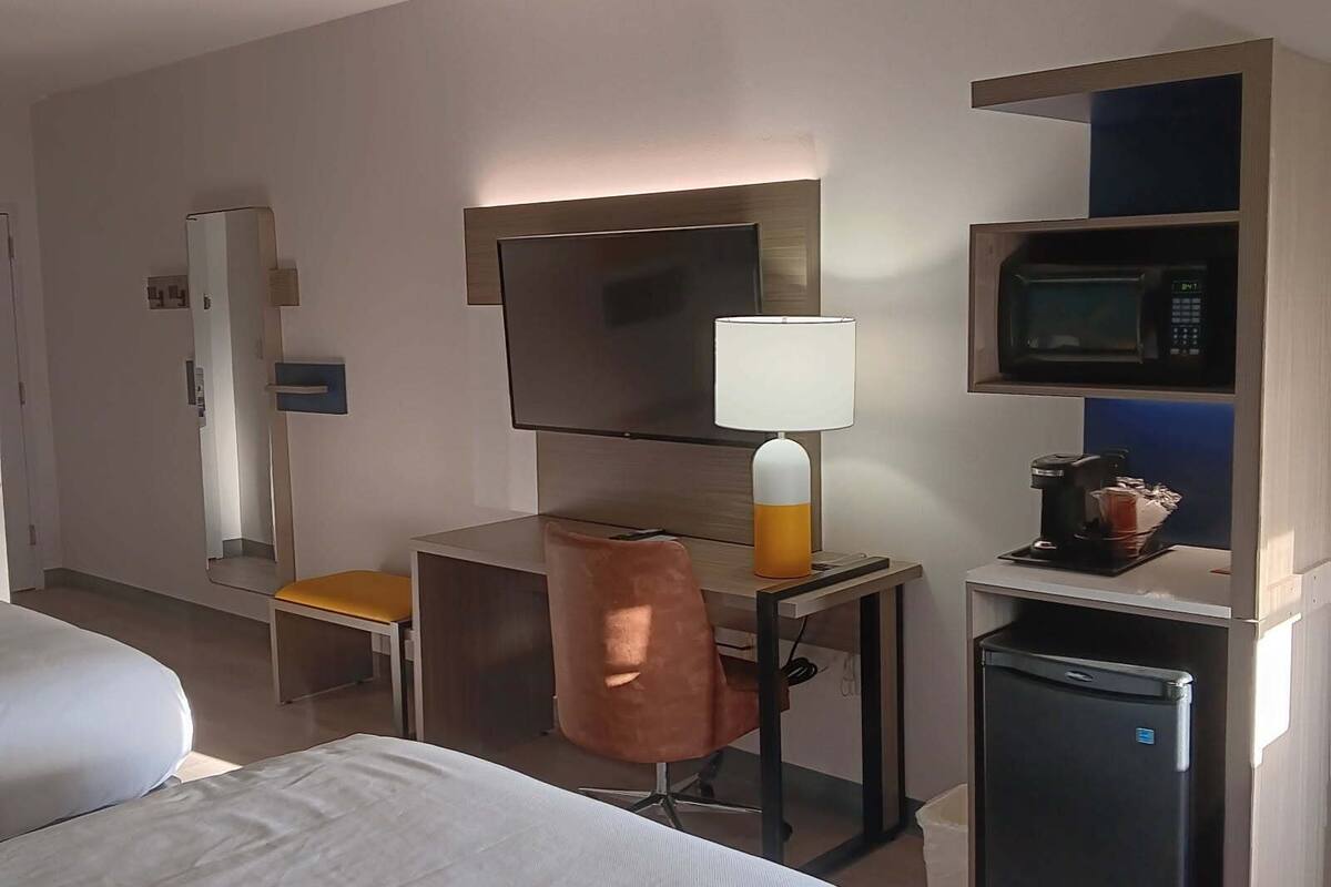 Ein Hotelzimmer mit zwei Betten, einem Schreibtisch mit Lampe, einer Mikrowelle und einem kleinen Kühlschrank.